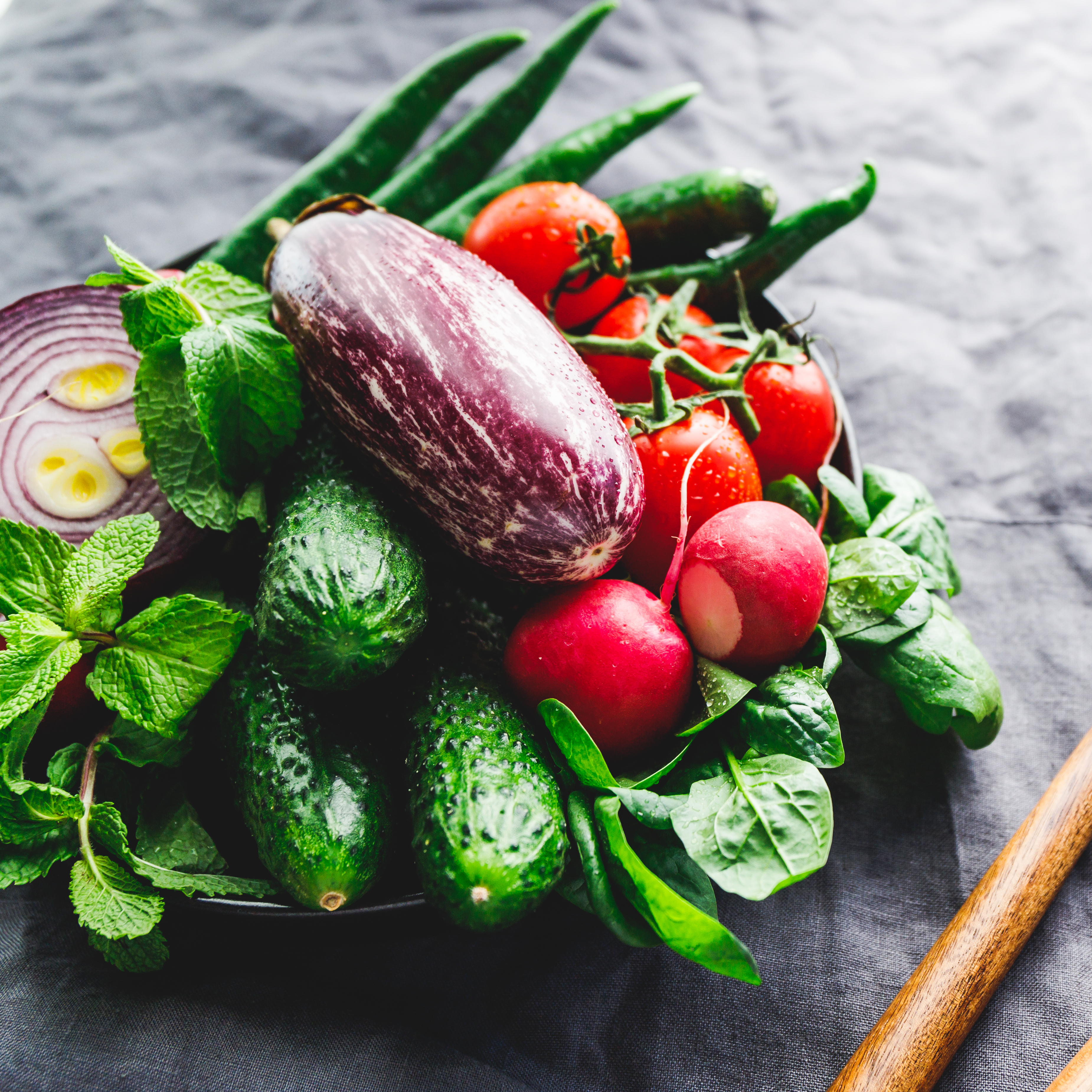 Various fresh colorful vegetables in a plate on a table with wooden kitchen utensils Various fresh colorful vegetables in a plate on a table with wooden kitchen utensils